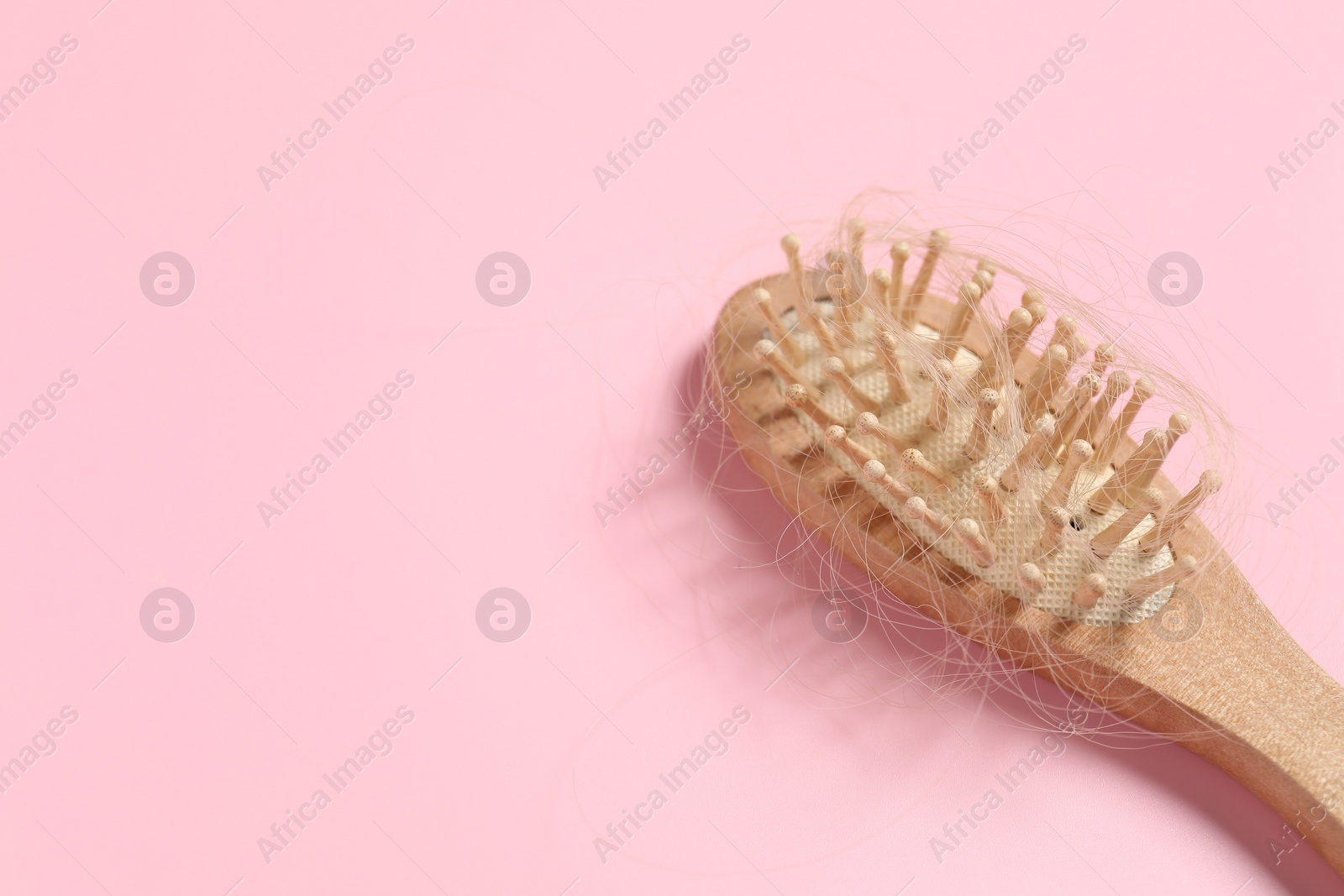 Photo of Wooden brush with lost hair on pink background, space for text