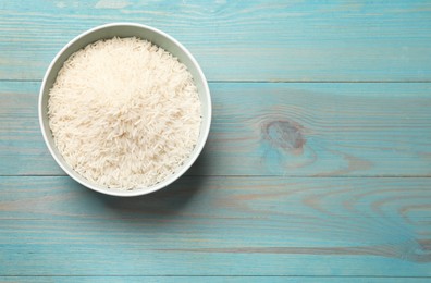 Photo of Raw basmati rice in bowl on light blue wooden table, top view. Space for text