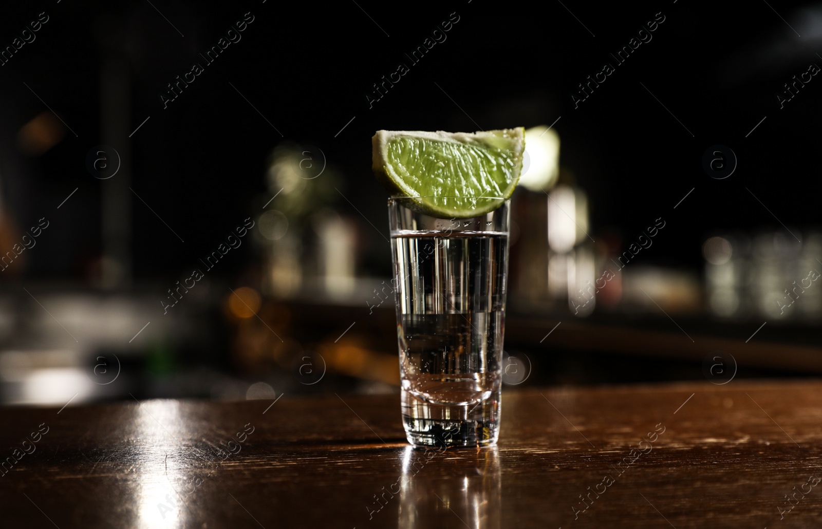 Photo of Mexican Tequila shot with lime slice on wooden bar counter