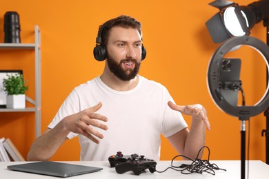 Photo of Smiling technology blogger with game controllers explaining something while recording video at home