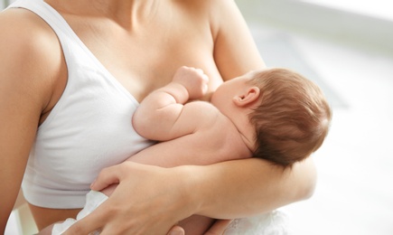 Photo of Young woman breastfeeding her baby on blurred background, closeup