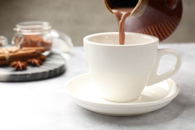 Photo of Pouring tasty hot chocolate into cup at light table, closeup. Space for text