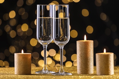 Photo of Champagne glasses and golden candles on table against defocused lights