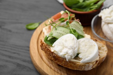 Photo of Tasty sandwich with burrata cheese, prosciutto and cucumber on grey wooden table, closeup