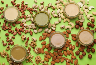 Photo of Different types of delicious nut butters and ingredients on light green background, flat lay