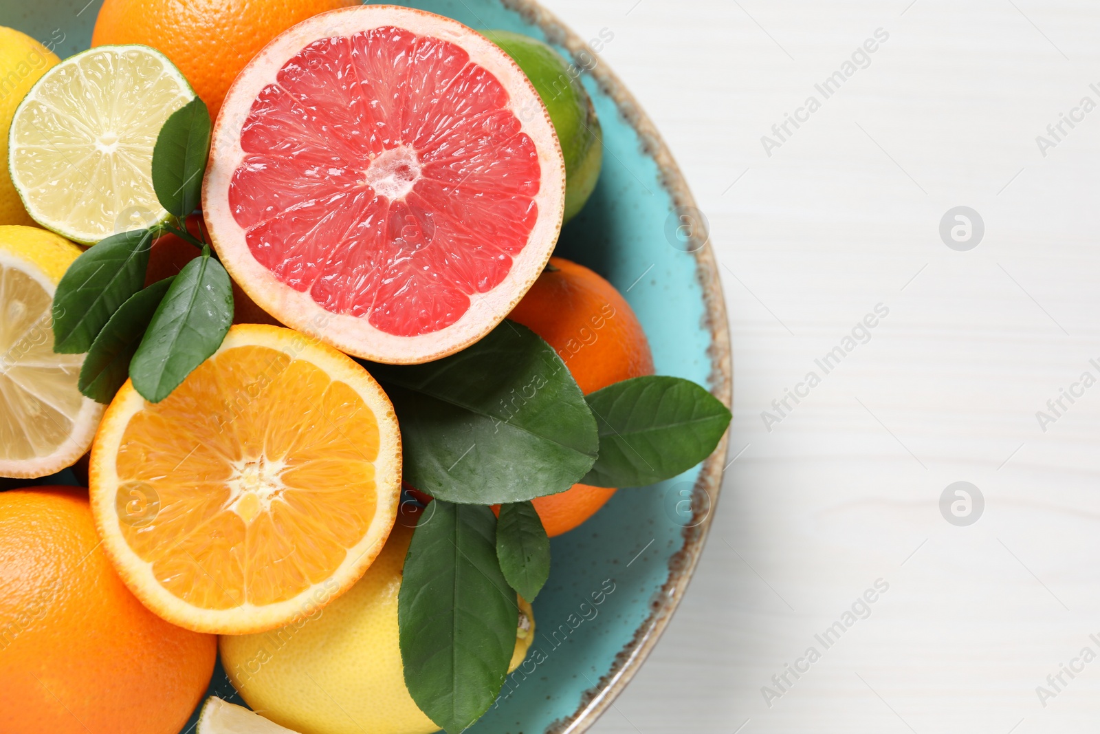 Photo of Different cut and whole citrus fruits on white wooden table, top view. Space for text