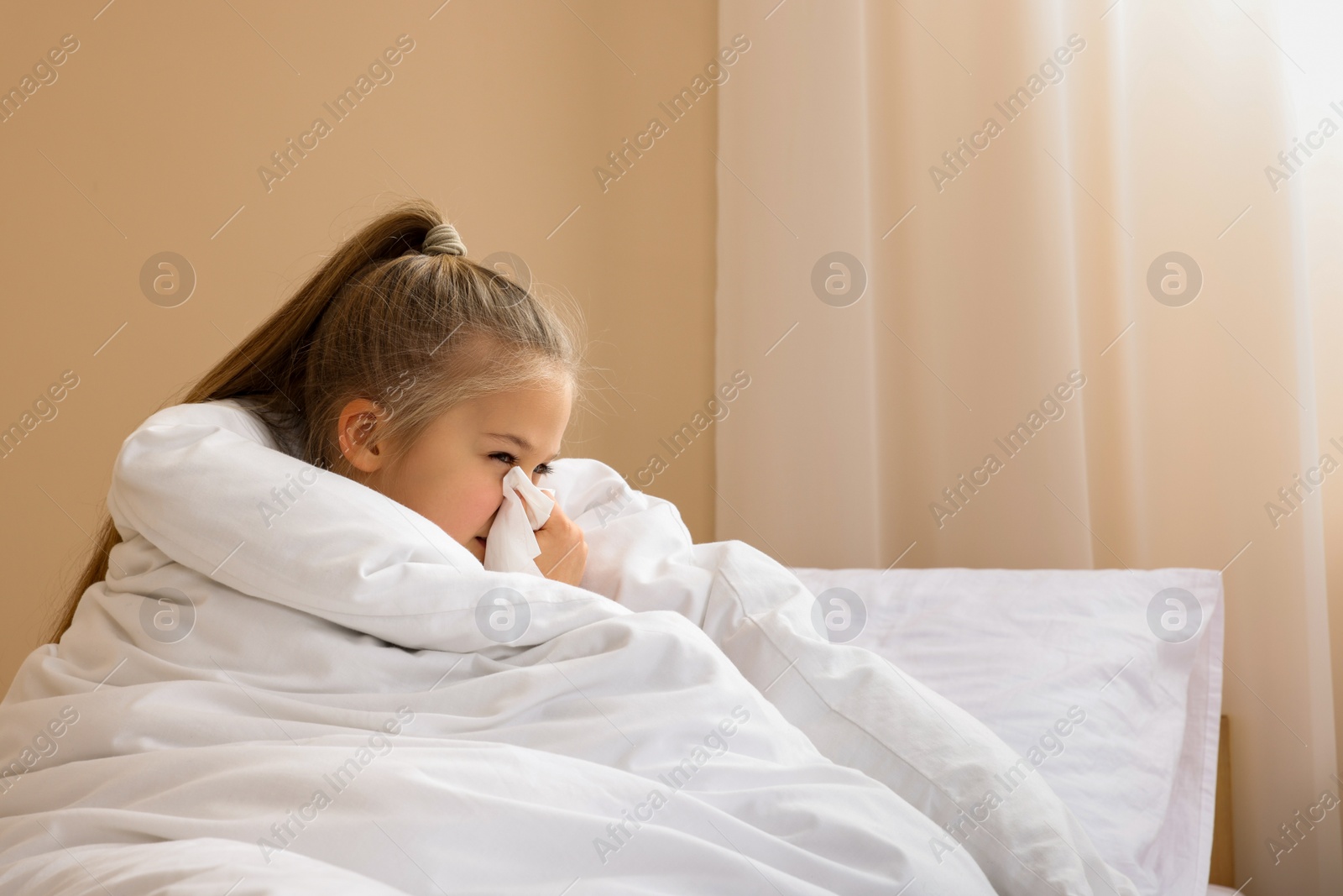 Photo of Sick girl with tissue blowing her nose in bed indoors, space for text. Cold symptoms