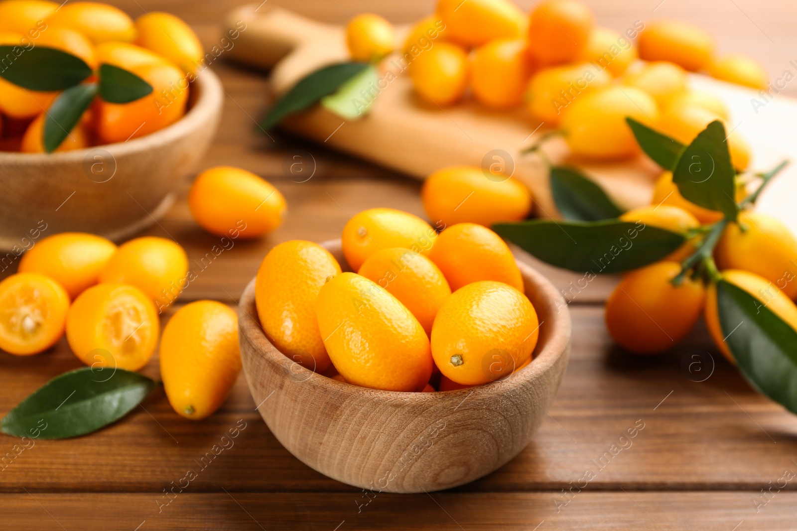 Photo of Fresh ripe kumquats with green leaves on wooden table