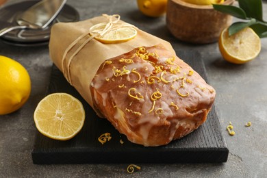 Photo of Wrapped tasty lemon cake with glaze and citrus fruits on grey table