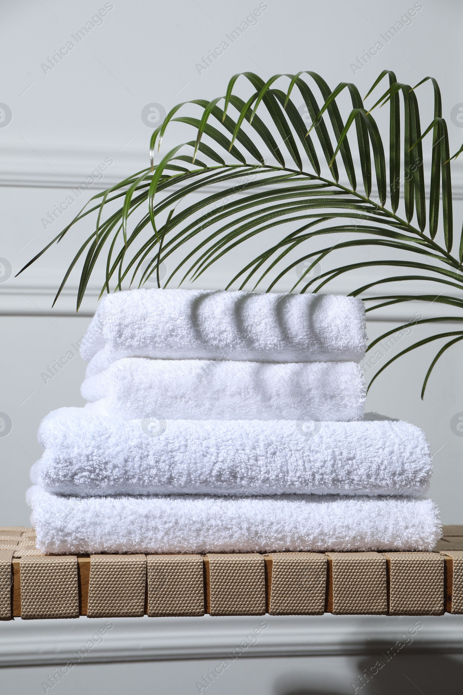 Photo of Stacked terry towels and green leaf on wicker bench indoors