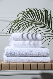 Stacked terry towels and green leaf on wicker bench indoors