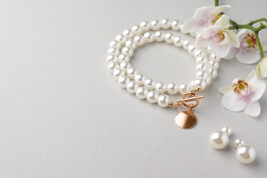 Photo of Elegant pearl necklace, earrings and orchid flowers on white background. Space for text