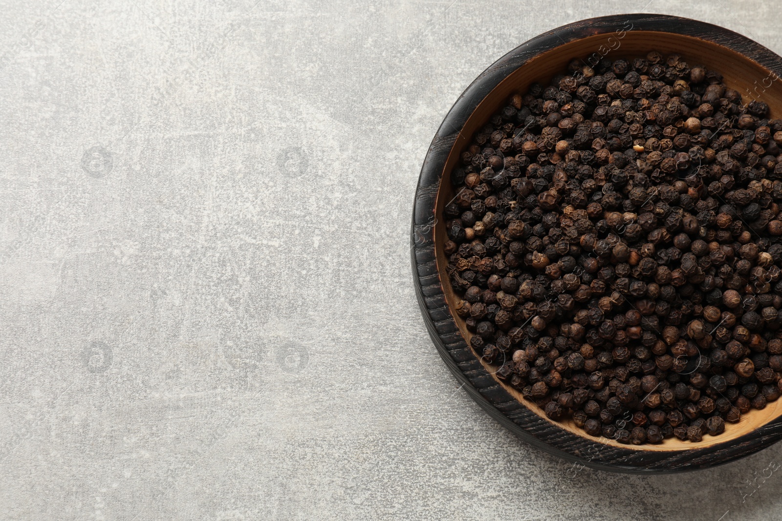 Photo of Aromatic spice. Black pepper in bowl on light grey table, top view. Space for text