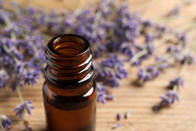 Bottle of essential oil and lavender flowers on wooden table, closeup. Space for text