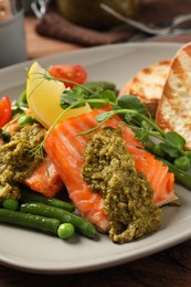 Photo of Tasty cooked salmon with pesto sauce served on wooden table, closeup