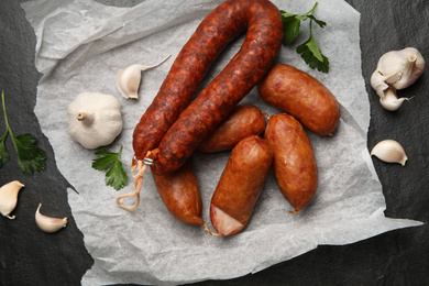 Photo of Delicious smoked sausages with garlic and parsley on black table, flat lay