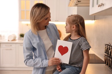 Photo of Little daughter congratulating her mom with greeting card in kitchen. Happy Mother's Day