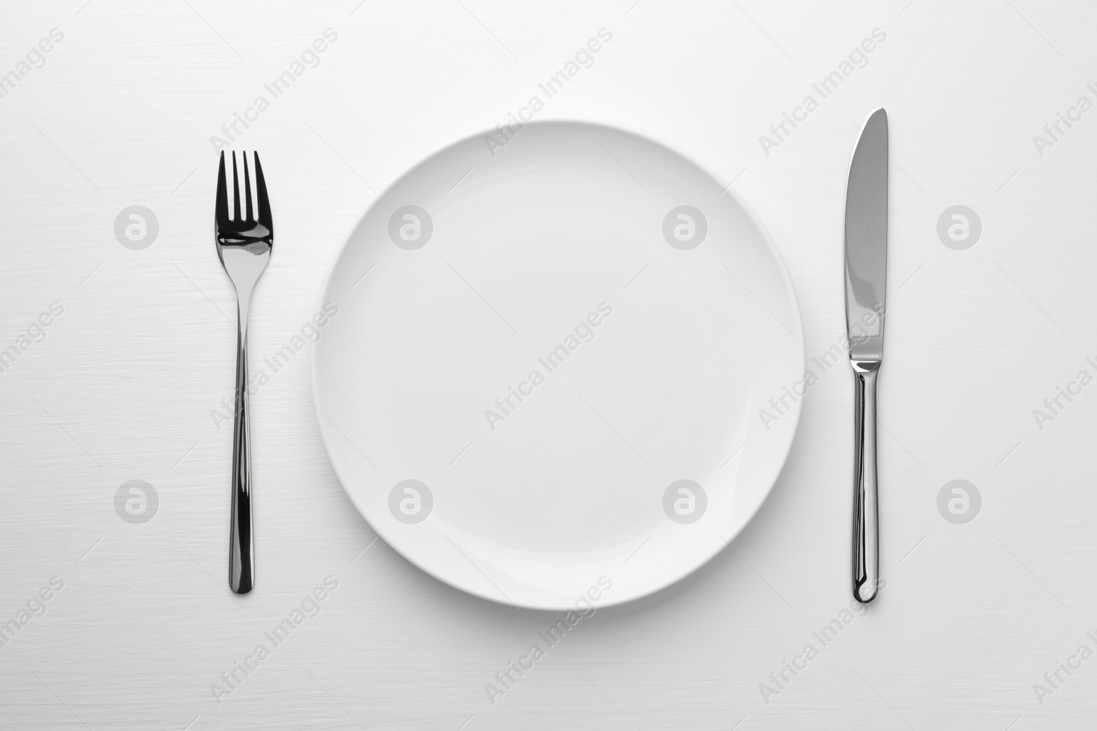Photo of Empty plate, fork and knife on white table, top view