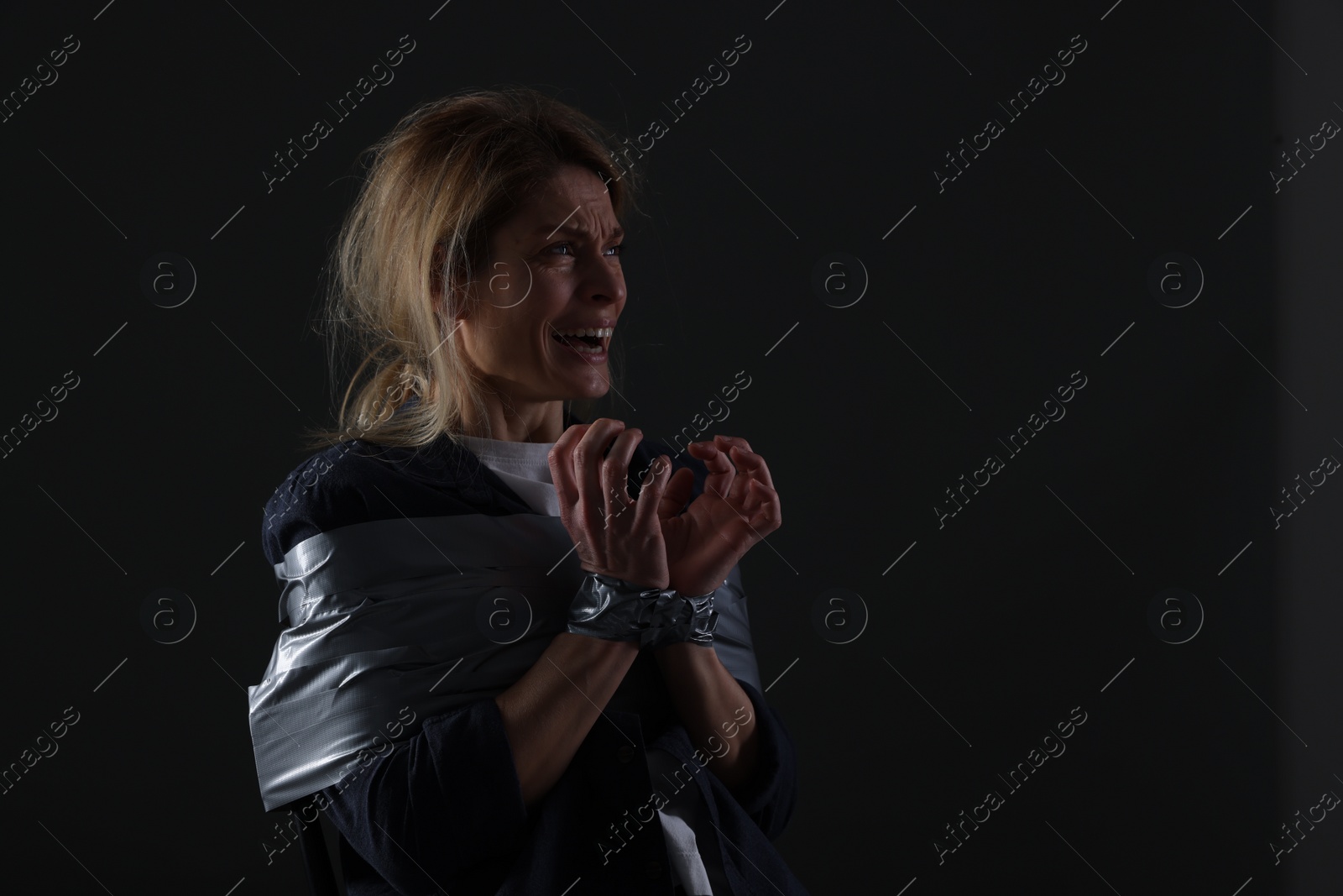 Photo of Scared woman taped up and taken hostage on dark background. Space for text