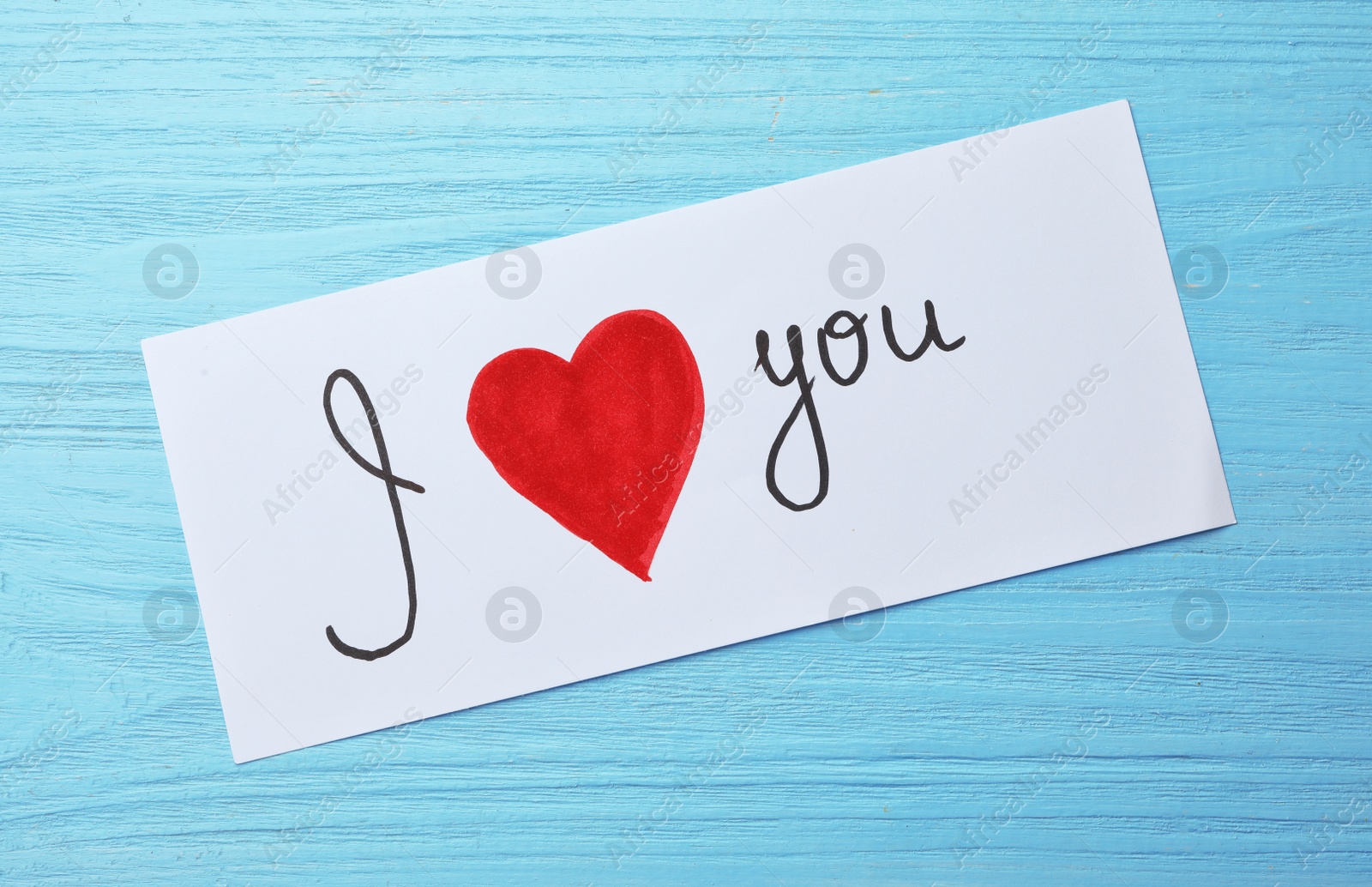 Photo of Paper sheet with words I LOVE YOU and heart on blue wooden table, top view