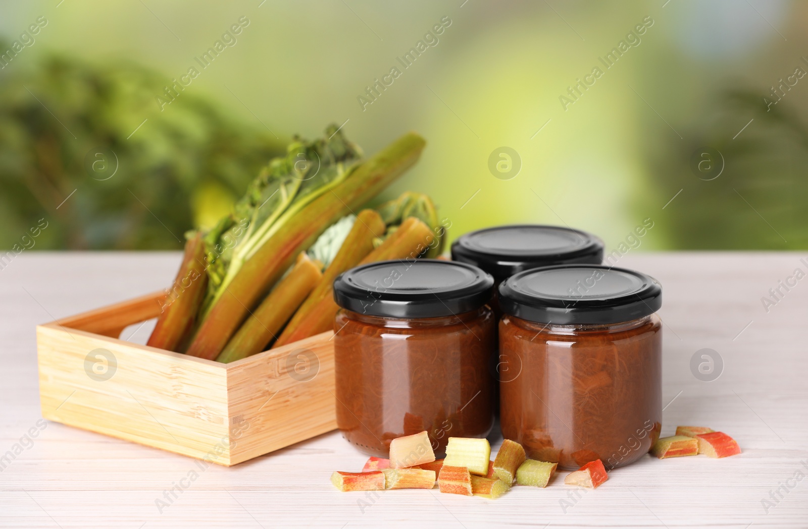 Photo of Jars of tasty rhubarb jam and stalks on white wooden table