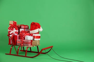 Sleigh with gift boxes and Santa's hat on green background. Space for text