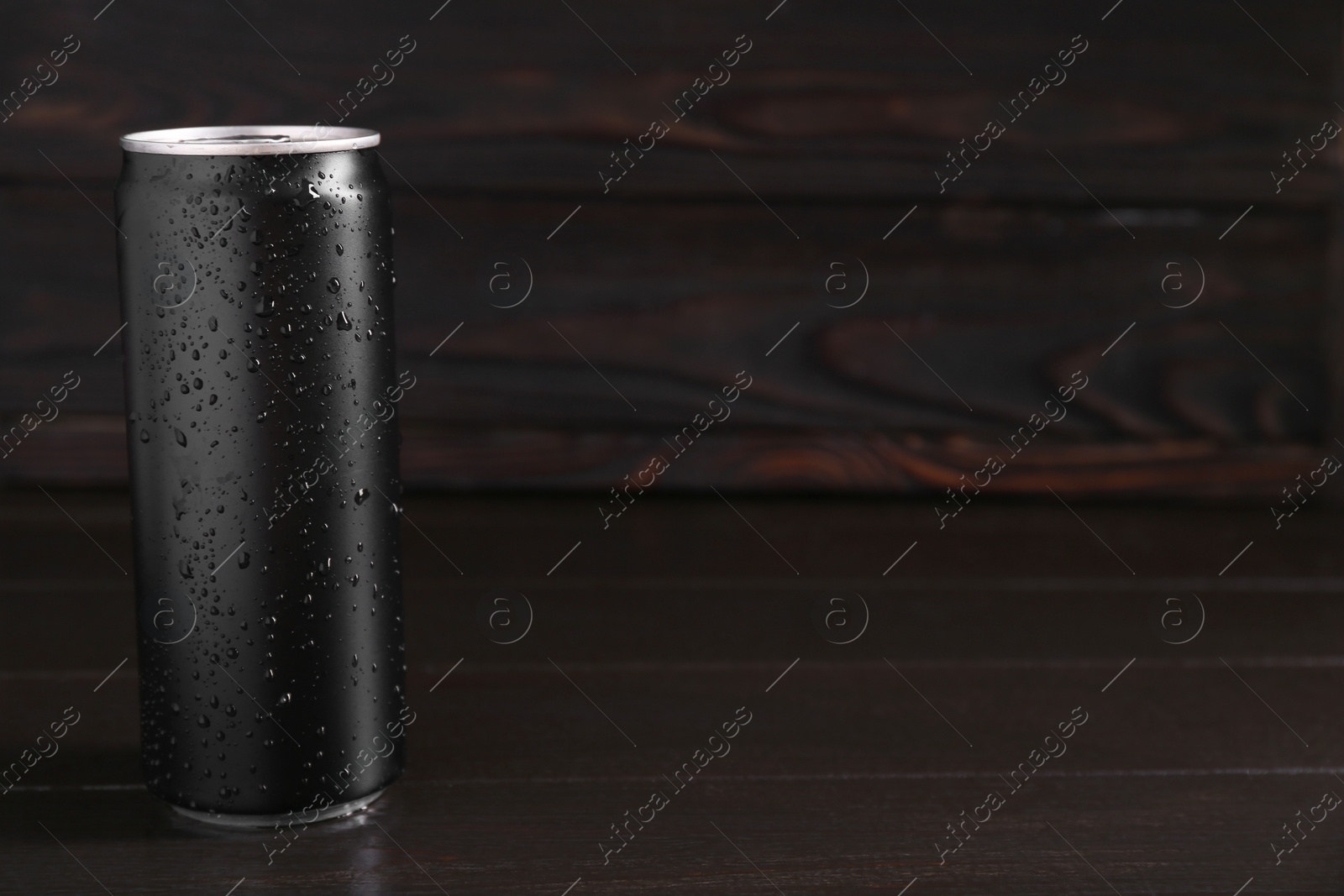 Photo of Energy drink in wet can on dark wooden table, space for text