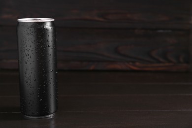 Energy drink in wet can on dark wooden table, space for text