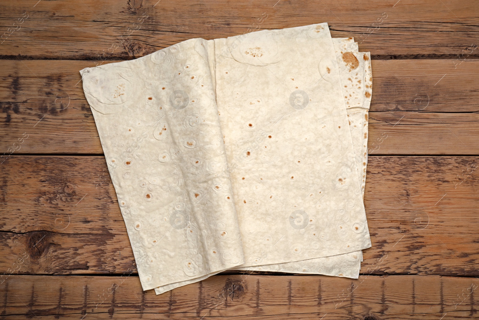 Photo of Delicious folded Armenian lavash on wooden table, top view