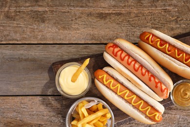 Delicious hot dogs with sauces and French fries on wooden table, top view. Space for text