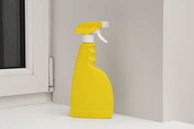 Photo of Yellow spray bottle of cleaning product on window sill indoors