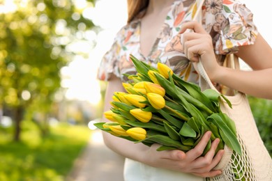 Photo of Teenage girl with bouquet of yellow tulips in park on sunny day, closeup. Space for text