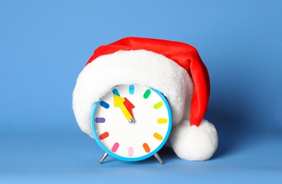 Photo of Alarm clock with Santa hat on blue background. New Year countdown