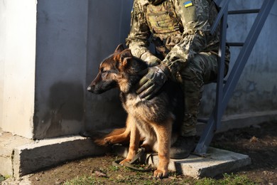 Photo of Ukrainian soldier with German shepherd dog sitting outdoors, closeup