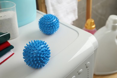 Blue dryer balls near stacked clean clothes and laundry detergents on washing machine. Space for text