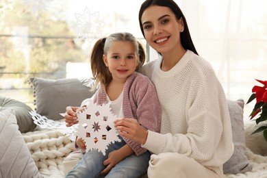 Mother and daughter with paper snowflake near window at home