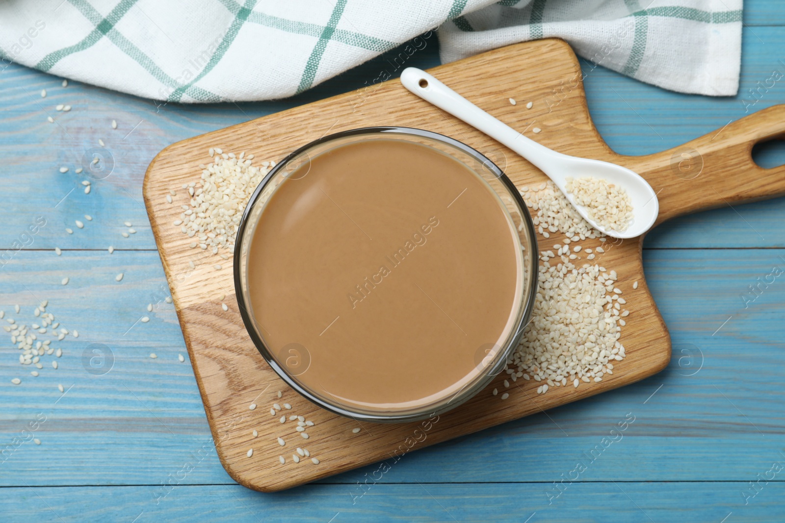 Photo of Tasty sesame paste, seeds and spoon on light blue wooden table, top view