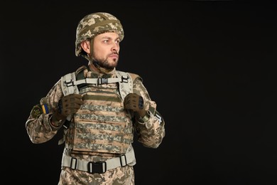 Soldier in Ukrainian military uniform on black background. Space for text