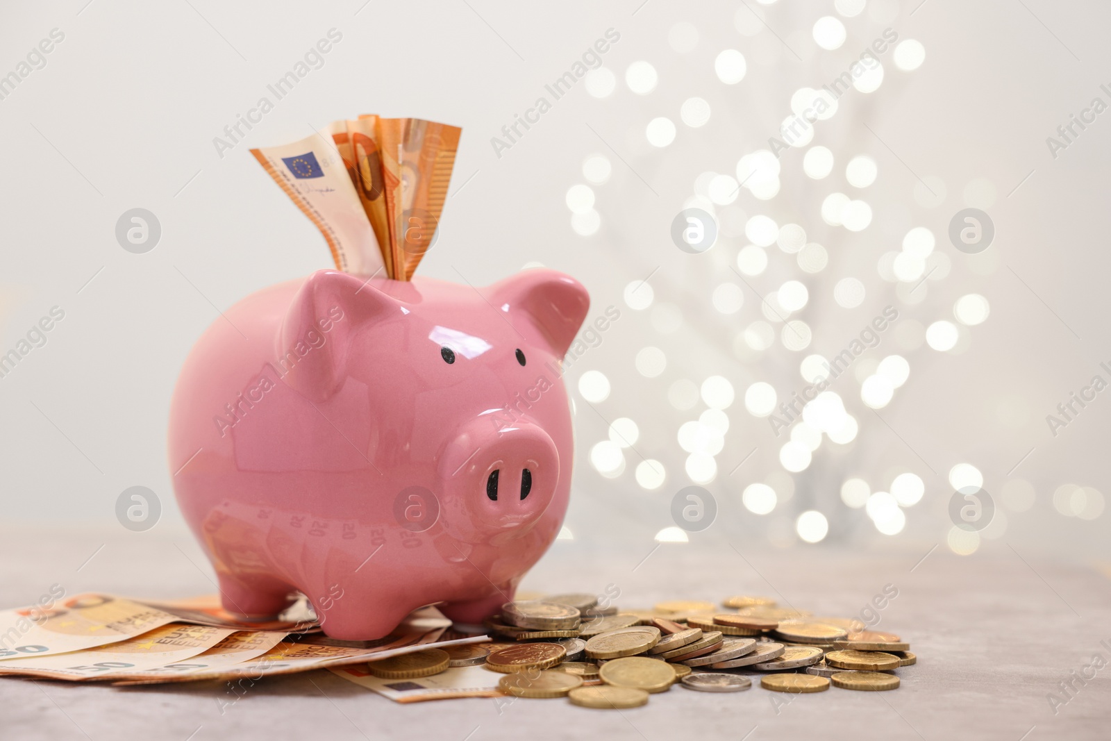 Piggy bank with euro banknotes and coins on grey table against blurred lights, space for text Photo of Piggy bank with euro banknotes and coins on grey table against blurred lights, space for text