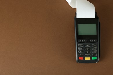 Photo of New modern payment terminal with blank paper bill on brown background, top view. Space for text