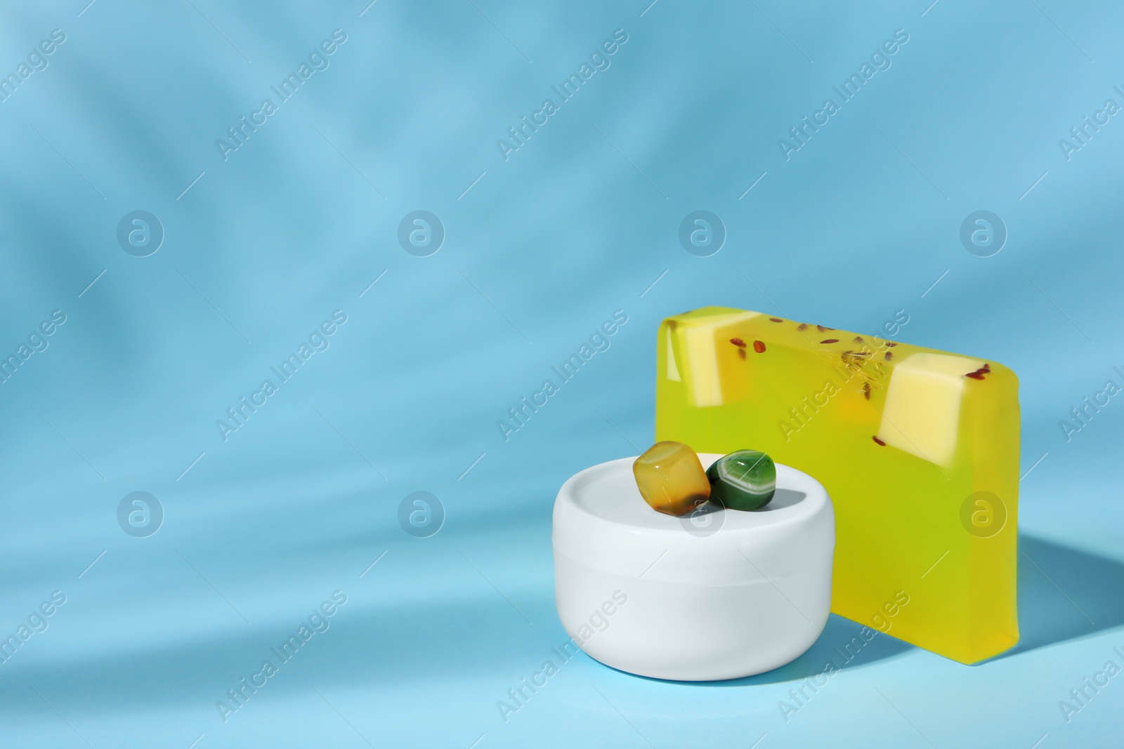 Photo of Cosmetic products and precious gemstones on light blue background. Space for text