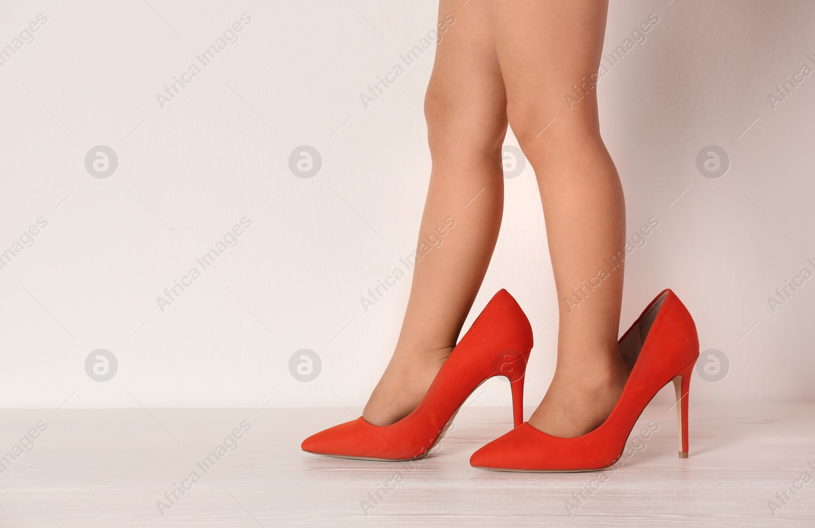 Photo of Little girl in oversized shoes near white wall with space for text, closeup on legs