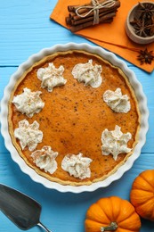 Photo of Delicious pumpkin pie with whipped cream and spices on light blue wooden table, flat lay