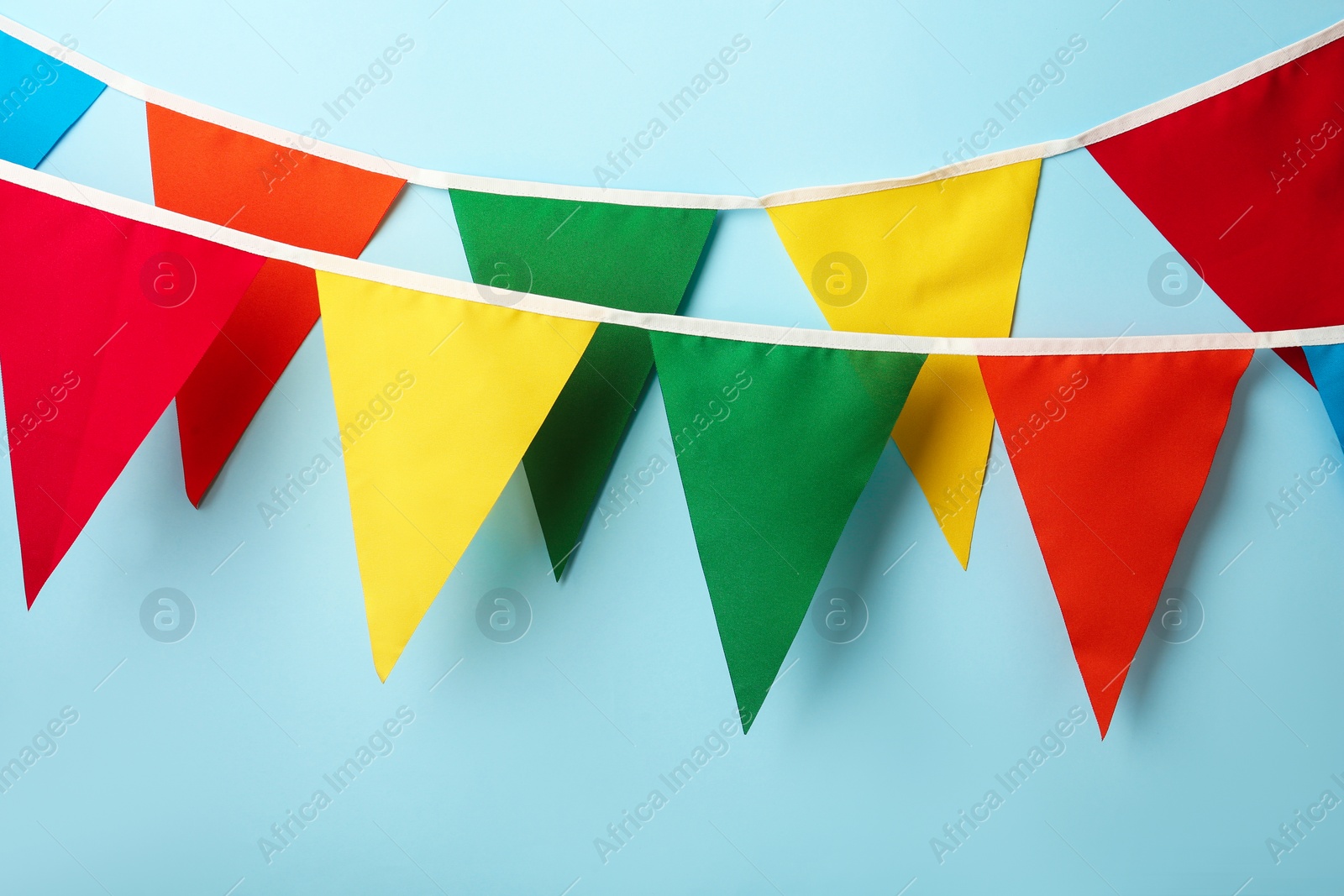 Photo of Buntings with colorful triangular flags hanging on light blue background. Festive decor