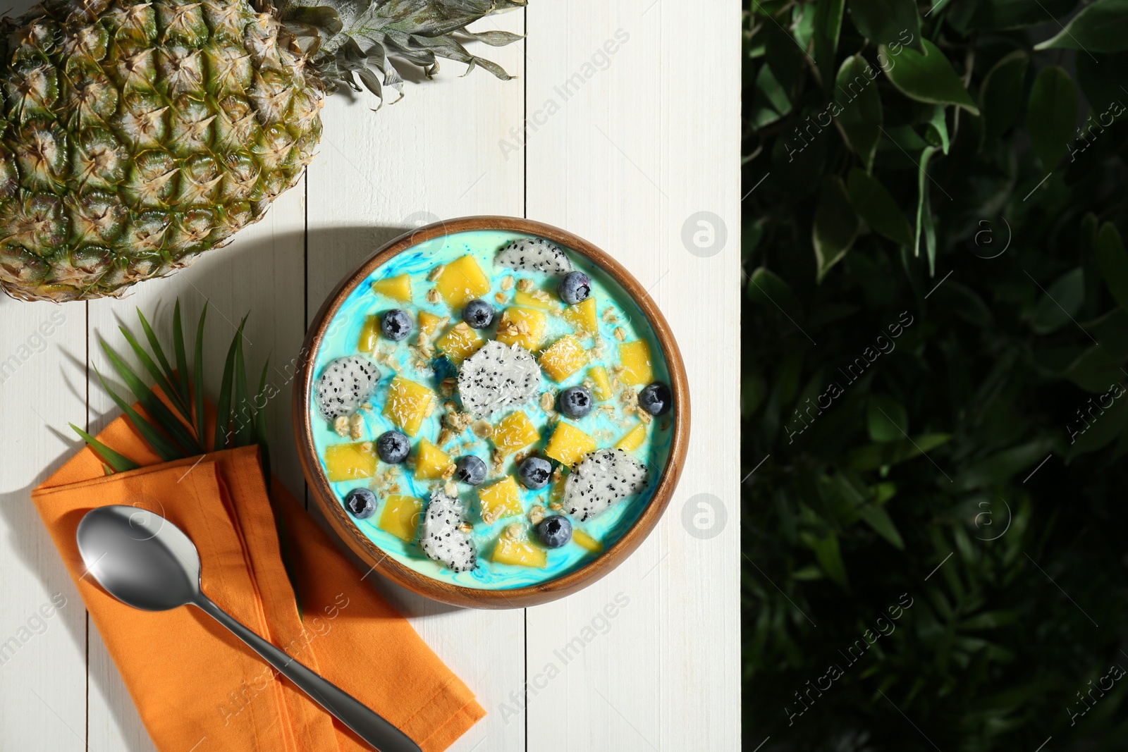 Photo of Delicious smoothie bowl with fresh fruits, blueberries and oatmeal served on white wooden table outdoors, flat lay. Space for text