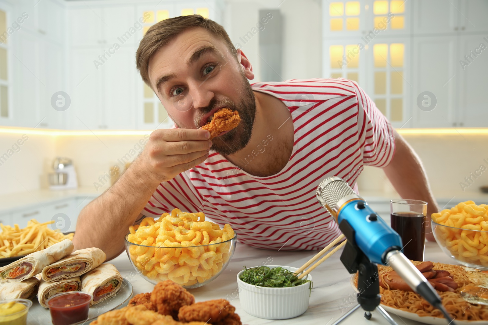 Photo of Food blogger eating near microphone at table in kitchen. Mukbang vlog