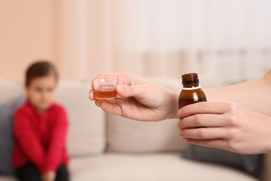 Photo of Mother with cough syrup for her daughter in room, focus on hands