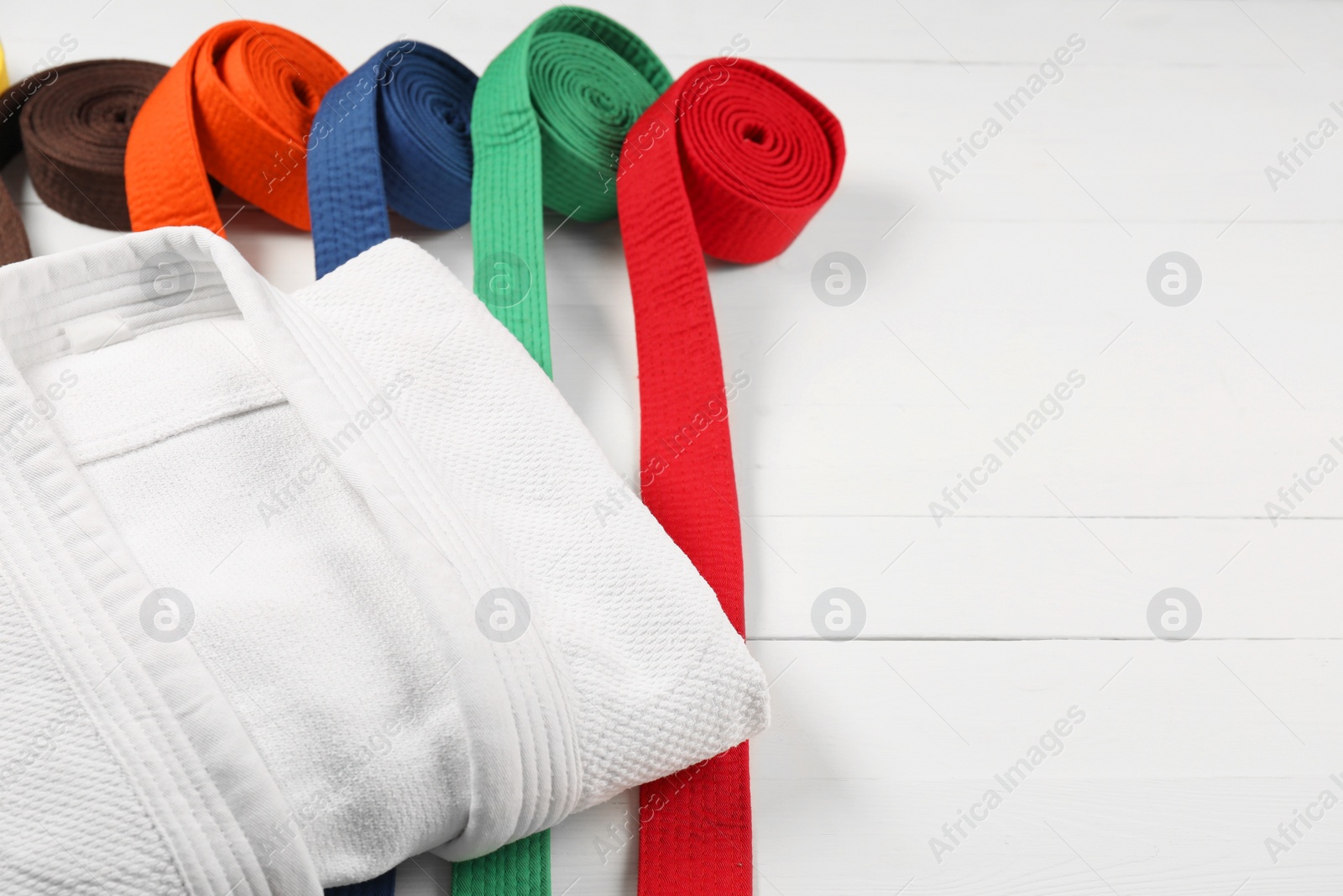 Photo of Colorful karate belts and white kimono on wooden background, closeup. Space for text