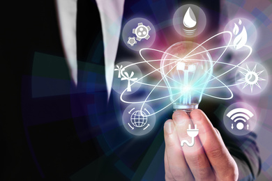 Image of Energy efficiency concept. Man holding light bulb surrounded by icons, closeup