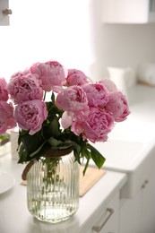 Vase with bouquet of beautiful pink peonies in kitchen